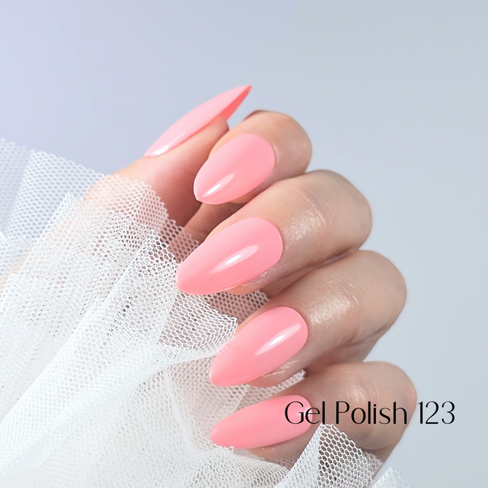 A gracefully posed hand displays almond-shaped nails painted in a soft, warm coral pink shade called Summer Romance. The gel polish has a smooth, high-gloss finish that reflects light beautifully. Delicate sheer white mesh fabric is draped over the fingers, adding a touch of elegance and femininity.
