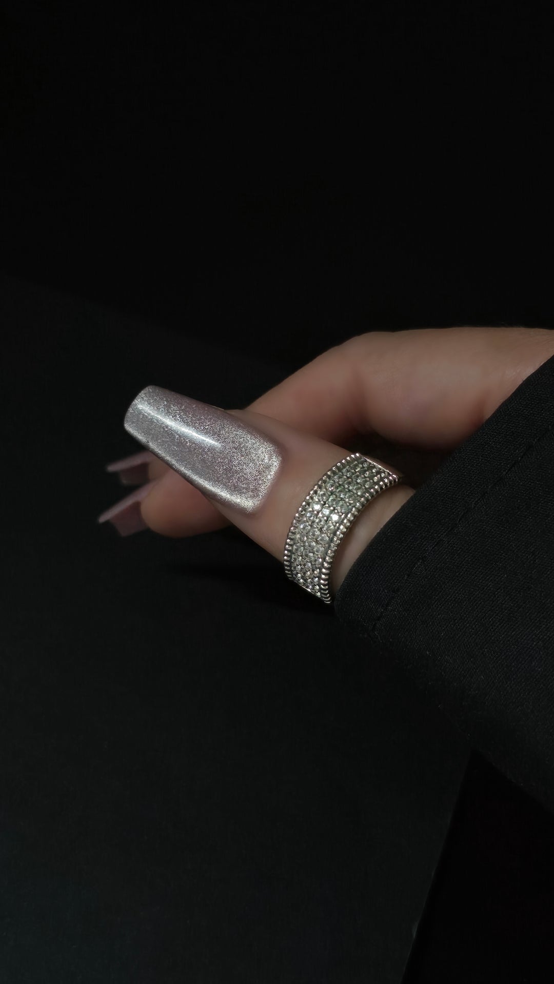 Close-up of silver cateye gel polish on long coffin nails, featuring a high-shine magnetic shimmer finish, perfect for luxury nail designs. Hand accessorized with rhinestone ring on a black background.