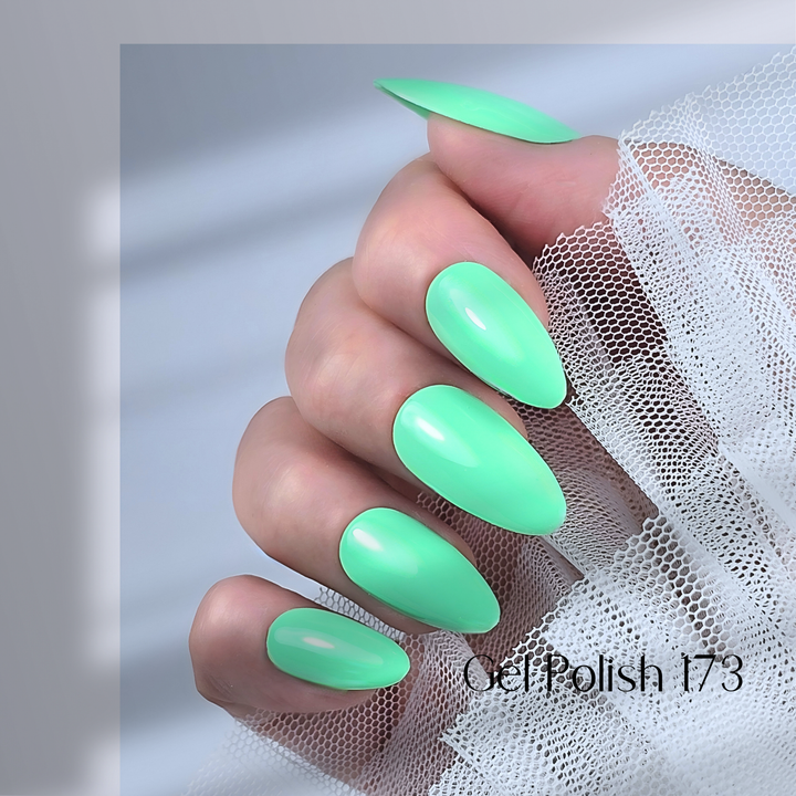 A close-up of a hand with long, almond-shaped nails painted in White Diamond Nails gel polish, shade 173. The polish features a bright, pastel mint green hue with a smooth, glossy finish. The hand is elegantly posed against delicate white lace fabric, creating a soft and sophisticated contrast.
