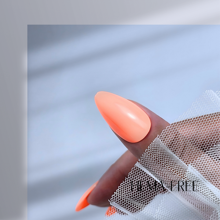 A close-up of a thumb painted in Peach Sorbet, shade 163, featuring a soft, creamy peach hue with a flawless, glossy shine. The nail is elegantly posed against delicate white lace fabric, adding a refined and elegant touch to the image.