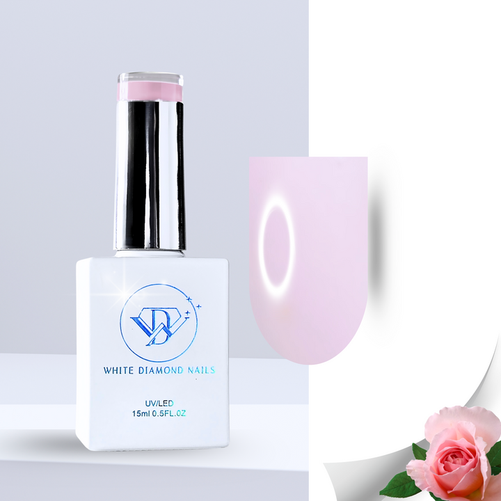 A delicate milky pink gel polish swatch with a dewy, translucent effect, applied to a clear nail tip. Resting over a floral arrangement of soft pink petals, glossy green leaves, and smooth white pebbles, this shade reflects a fresh, rose-scented elegance.