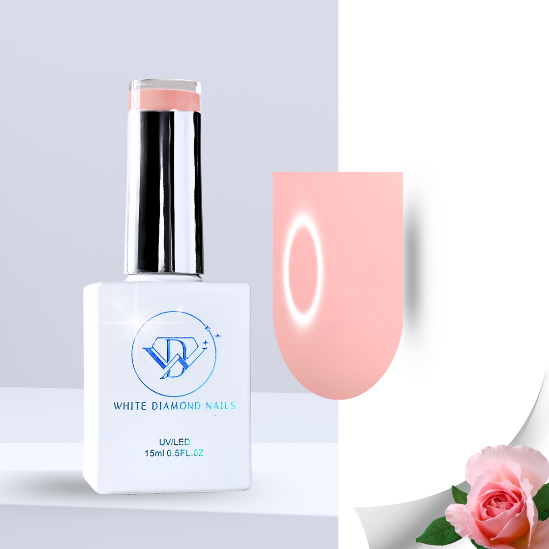 A warm peachy-pink gel polish swatch with a creamy, high-shine finish, applied on a clear nail tip. The background features fresh pink rose petals, water-dappled green leaves, and soft white pebbles, enhancing the cozy and romantic appeal of this rose-scented shade.