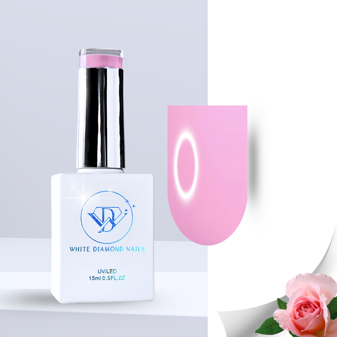 A romantic soft pink gel polish swatch on a clear nail tip with a creamy, full-coverage finish. The background showcases fresh pink rose petals, dewy green leaves, and white pebbles in water, complementing the floral elegance of this rose-scented polish.