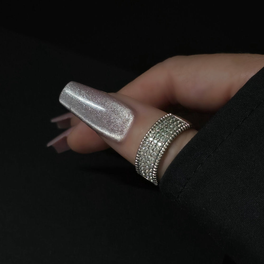 Close-up of silver cateye gel polish on long coffin nails, featuring a high-shine magnetic shimmer finish, perfect for luxury nail designs. Hand accessorized with rhinestone ring on a black background.