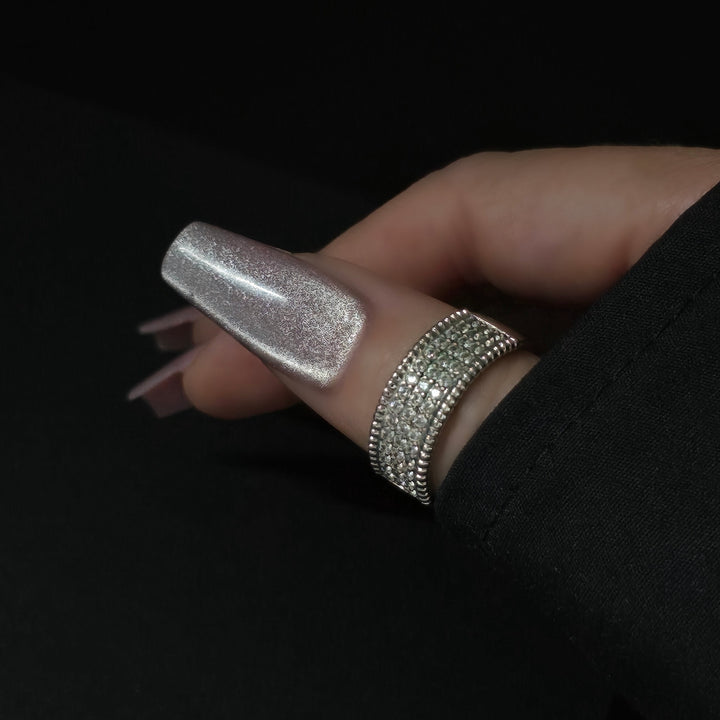 Close-up of silver cateye gel polish on long coffin nails, featuring a high-shine magnetic shimmer finish, perfect for luxury nail designs. Hand accessorized with rhinestone ring on a black background.