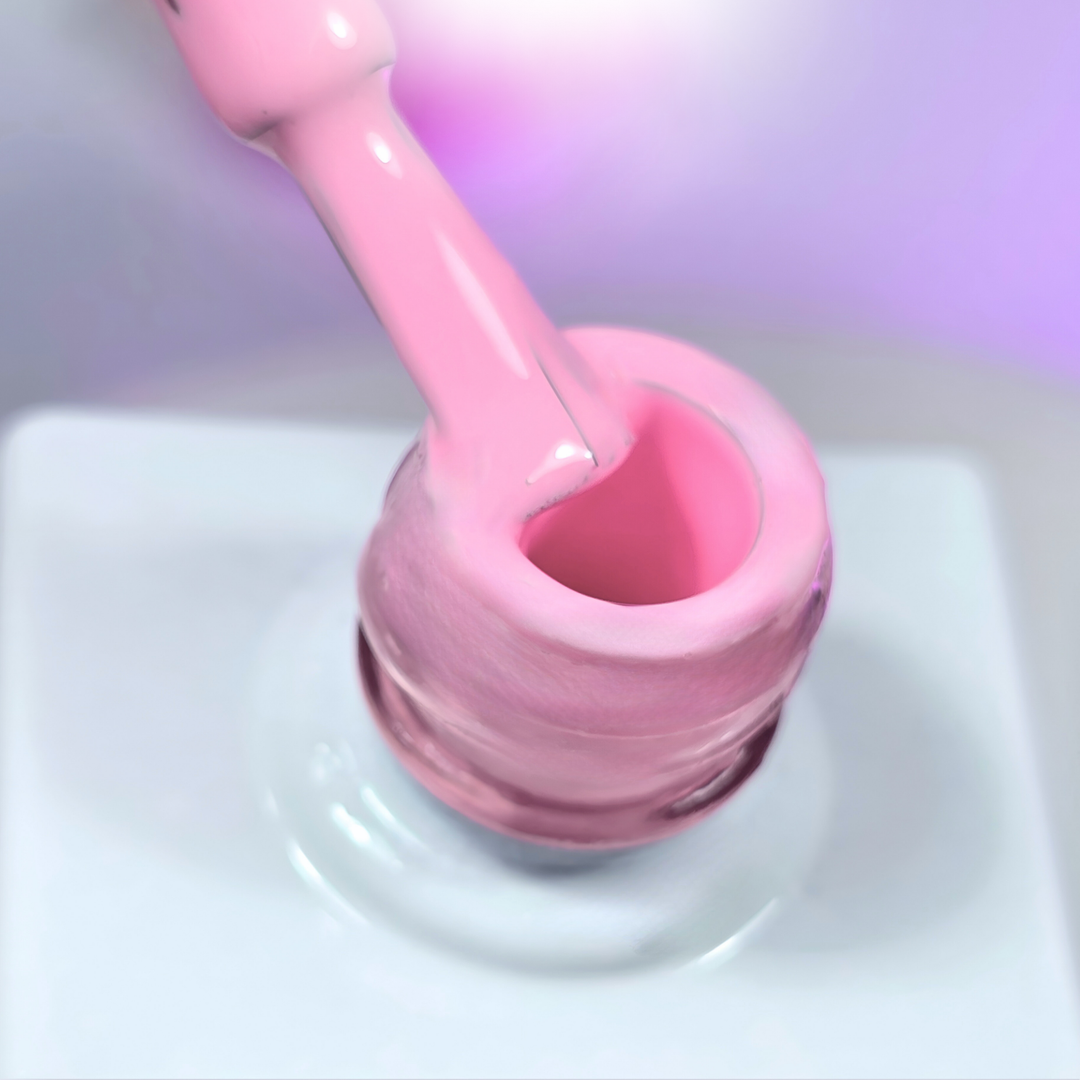 A pastel pink gel polish being lifted from the bottle with a brush, revealing its smooth and self-leveling consistency. The background features a soft purple glow, adding to the polish’s delicate and feminine aesthetic.